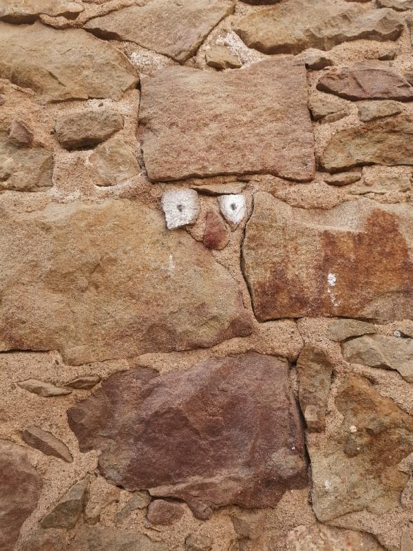 Dos ojos en una pared de piedra forman una cara sin boca / Dos ulls en una paret de pedra formen una cara sense boca